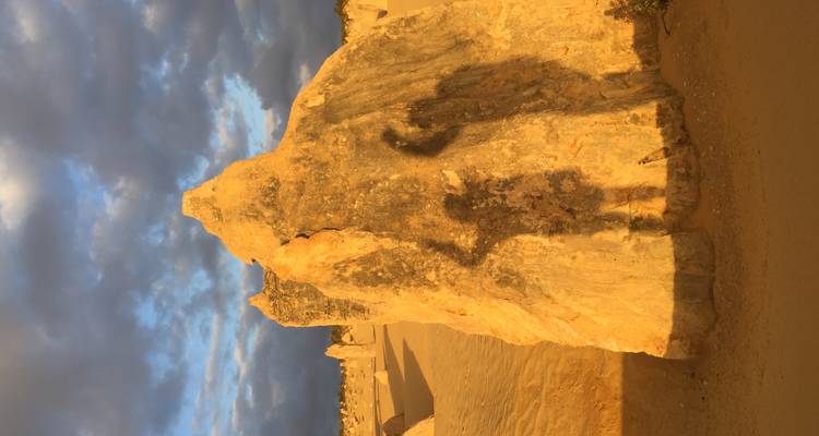 Sunlit limestone pinnacle casting tall shadows across a desert landscape under dramatic clouds