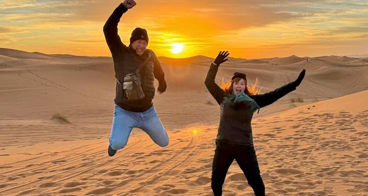Zwei Menschen, die vor Freude in der Sahara-Wüste bei Sonnenuntergang springen.