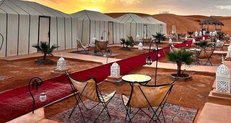 A luxury desert camp with tents and decorative seating at sunset.