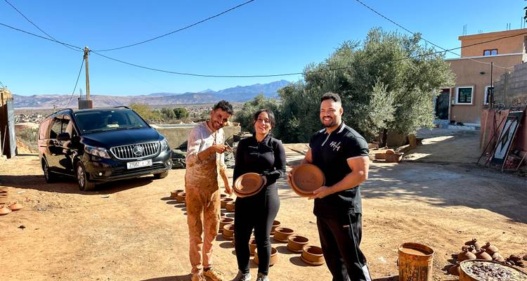 Drei Personen halten Töpferwaren in einem offenen Hof mit Bergen im Hintergrund.