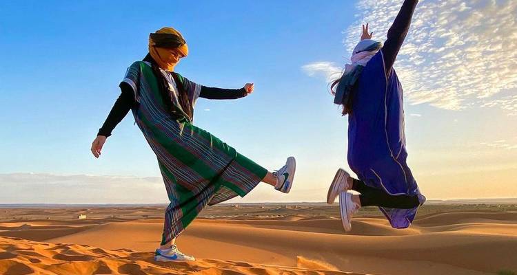 Zwei Menschen in traditioneller Kleidung springen in der Wüste.