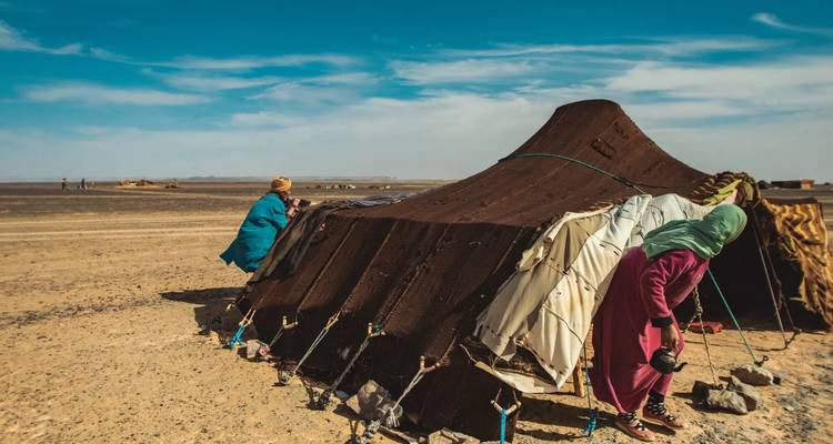 Zwei Personen bauen ein großes Stoffzelt in der Wüste auf.