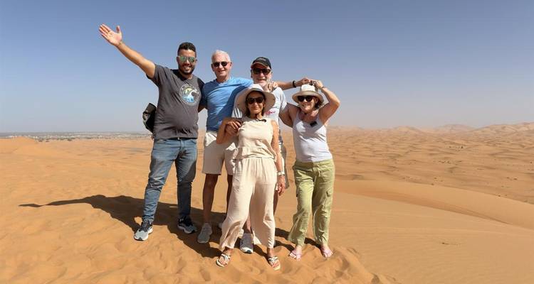 Grupo de viajeros posando en dunas doradas bajo un cielo desértico despejado.