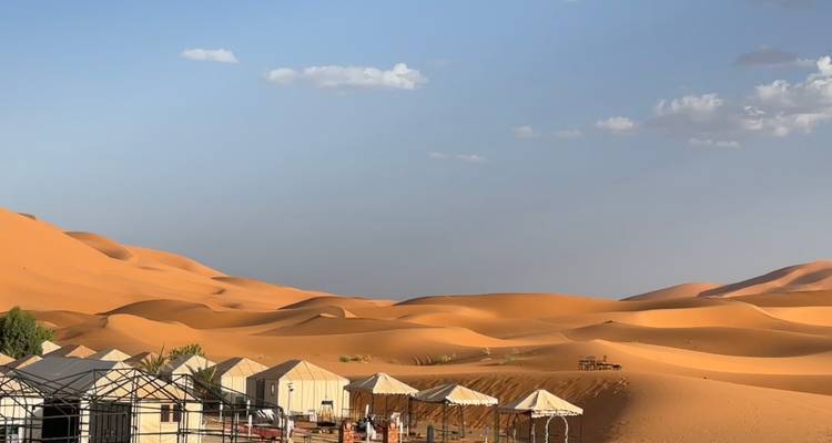 Hileras de tiendas de campaña beige del desierto y asientos sombreados se encuentran entre dunas naranjas ondulantes bajo un cielo despejado.