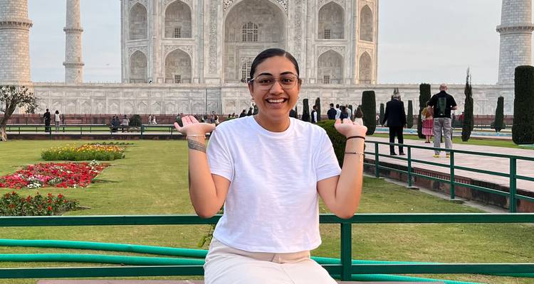 Glimlachende reiziger poseert met opgeheven handen voor weelderige tuinen en de Taj Mahal.