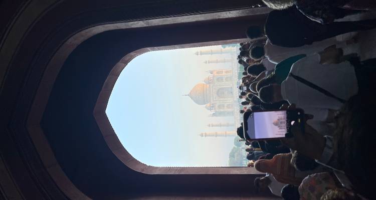 Menigte loopt door gebogen poort die de verre Taj Mahal omlijst, een telefoon legt de scène vast.
