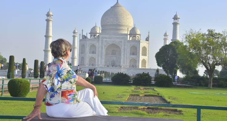 Vrouw zit op een bankje en geniet van het uitzicht op de Taj Mahal over verzorgde tuinen heen in het heldere ochtendlicht