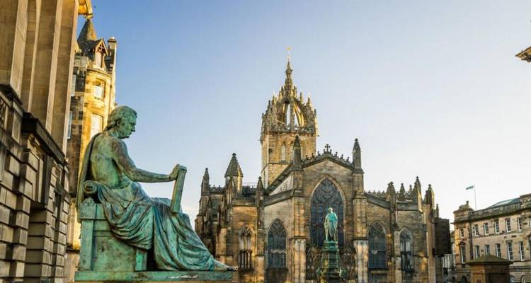 Standbeeld van een filosoof met op de achtergrond de Sint-Giliskerk en historische gebouwen van de oude stad in Edinburgh.