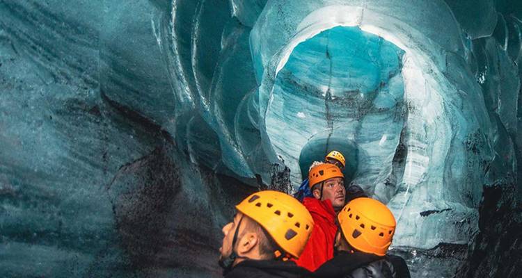 Aventureros con cascos exploran el interior azul vibrante de una cueva de hielo islandesa.