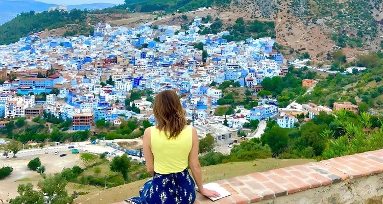 El viajero se sienta en una cornisa con vista a las extensas casas azules de Chefchaouen respaldadas por colinas verdes