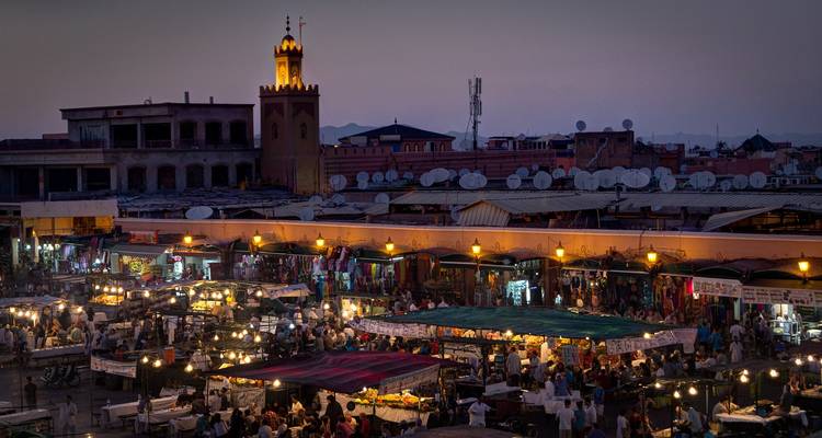 De nacht valt over Jemaa el-Fna waar marktlichten fonkelen onder een paarse lucht en een moskee minaret