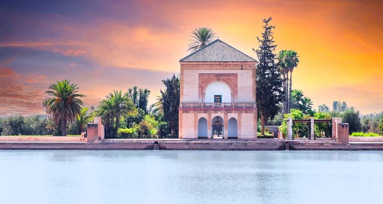 Menara paviljoen weerspiegeld in stil water onder een levendige zonsonderganghemel met palmbomen die de scène omlijsten