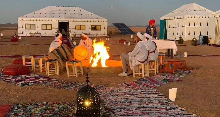Des musiciens traditionnels se rassemblent autour d'un feu de camp près de tentes berbères sur le sable du Sahara au crépuscule.