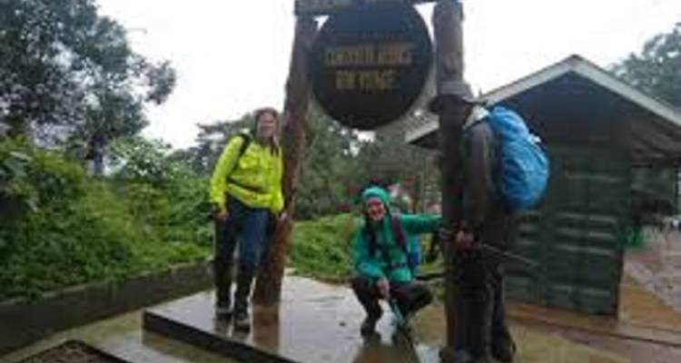 Three hikers posing at a Kilimanjaro National Park sign.