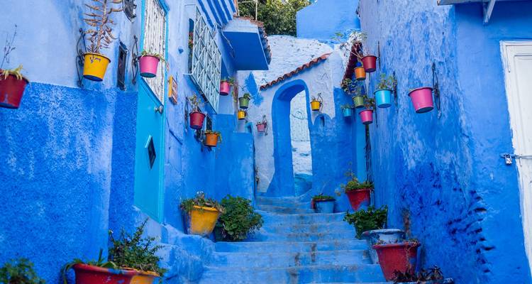 Una calle estrecha bordeada de edificios pintados de azul y macetas coloridas en Chefchaouen, Marruecos.