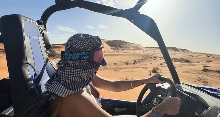 Un aventurier conduisant un buggy bleu à travers les dunes de sable doré du Sahara sous un soleil d'après-midi brillant.