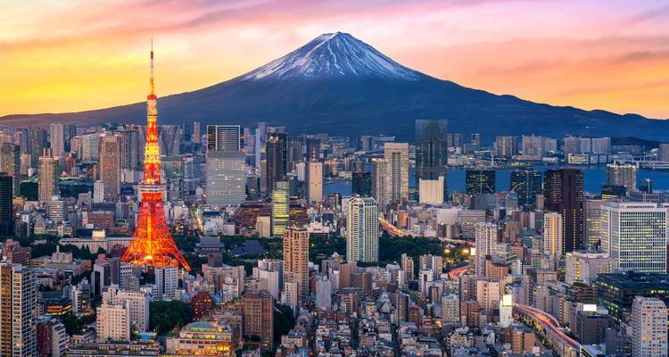 El horizonte de Tokio al atardecer con la Torre de Tokio brillantemente iluminada y el Monte Fuji cubierto de nieve brillando en los colores del atardecer.