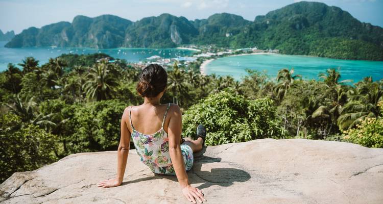 Person relaxing on a rock overlooking a tropical bay.