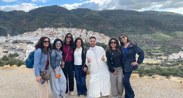 Groupe de voyageurs souriants avec un guide local posant sur une crête surplombant une ville de colline colorée au Maroc