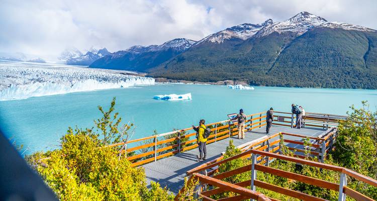 Des touristes observant un glacier et des montagnes depuis une plateforme d'observation.