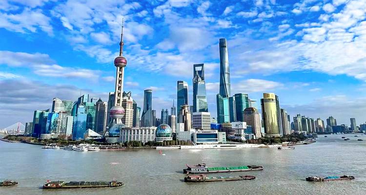 Helder daglicht panorama van de skyline van Shanghai Pudong met iconische wolkenkrabbers die achter de brede Huangpu-rivier uitsteken, waar scheepsbarges voorbijvaren.