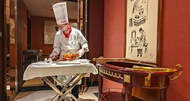Chef in traditionele witte kleding die aan tafel een geroosterde Pekingse eend uitsneidt in een chic Chinees restaurant.