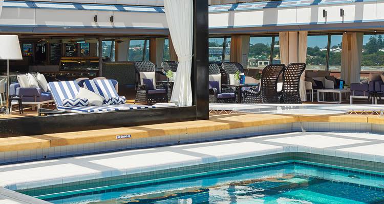 Een luxueus cruiseschip dek met een zwembad en ligstoelen.