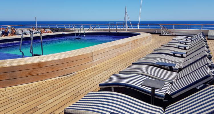 Cruiseschip dek met een zwembad en ligstoelen.