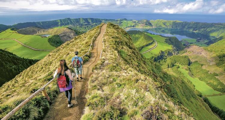 Wandelaars die een bergkampad verkennen met uitgestrekte uitzichten op valleien en meren.