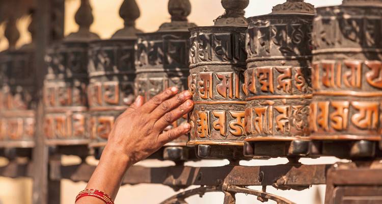 Hand touching prayer wheels lined up for spinning.