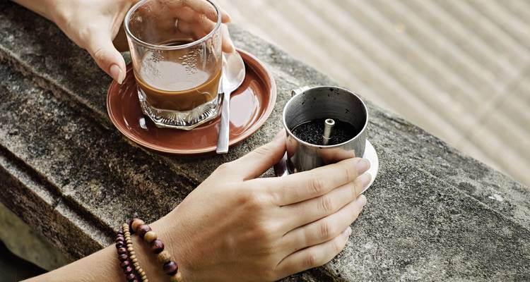 Hands holding coffee cup and filter on a stone ledge.
