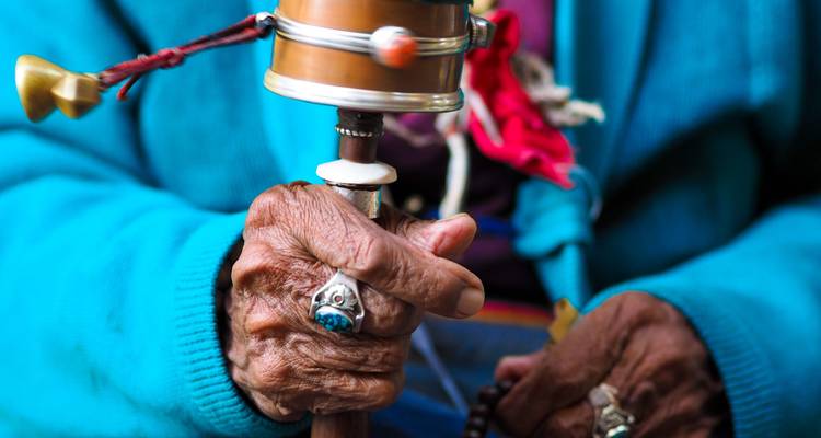 Nahaufnahme von älteren Händen, die ein Gebetsrad halten.