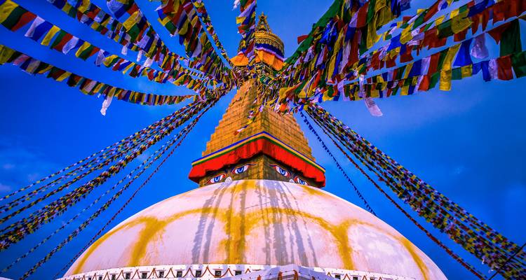 Banderas de oración coloridas alrededor de una estupa con un cielo vibrante y despejado.