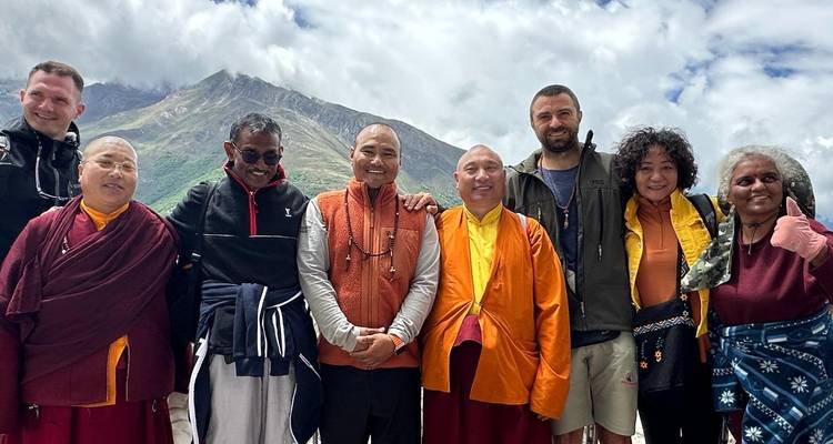 Grupo de personas posando en colorida vestimenta tradicional y casual con un fondo escénico de montañas.