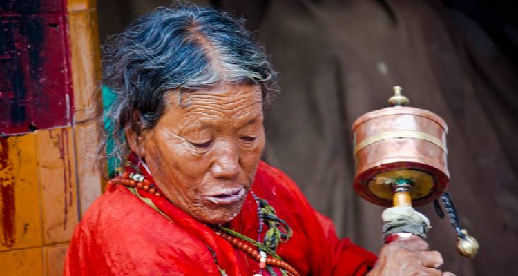 Mujer anciana en atuendo tradicional con una rueda de oración.