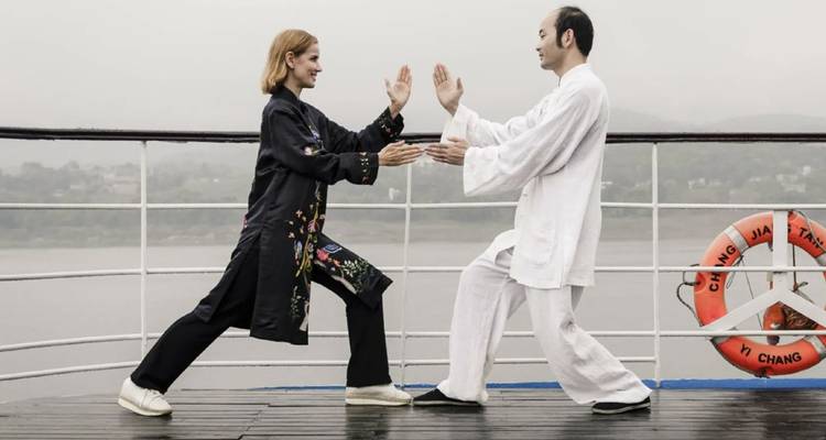 Dos pasajeros practicando tai chi en la cubierta de un crucero fluvial con clima brumoso.