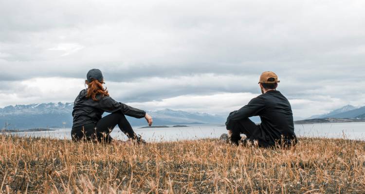 Deux personnes assises sur un champ herbeux avec un paysage montagneux en arrière-plan.