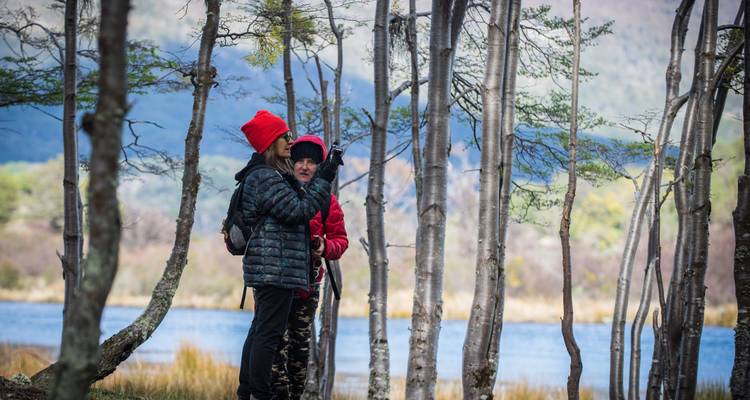 Deux personnes en vêtements chauds se tenant debout parmi des arbres près d'un plan d'eau.