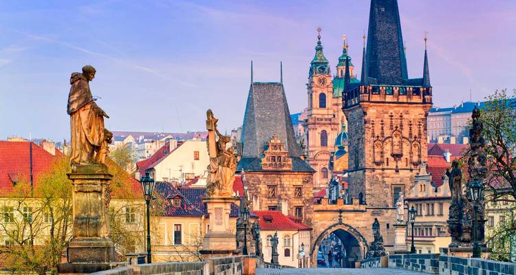 Historic bridge with statues and towers at sunrise.