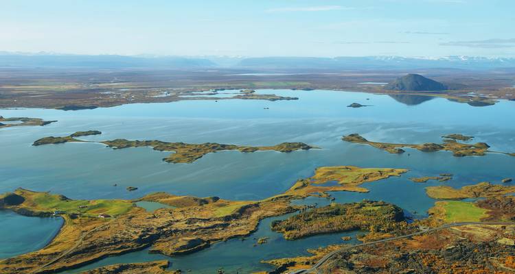 Vue aérienne panoramique des îlots volcaniques du lac Mývatn et de ses eaux miroirs entourées de toundra automnale et de montagnes lointaines.