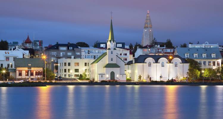 Die Abendlichter spiegeln sich im Tjörnin-See von Reykjavik wider, mit der Fríkirkjan-Kirche und dem Hallgrímskirkja-Turm in der Ferne.