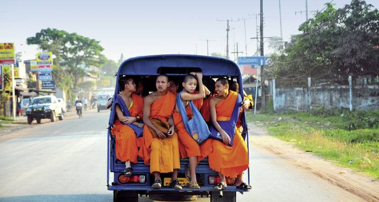 A group of young monks riding in an open vehicle on a street.