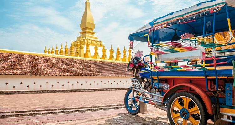 A colorful tuk-tuk parked in front of a golden temple.