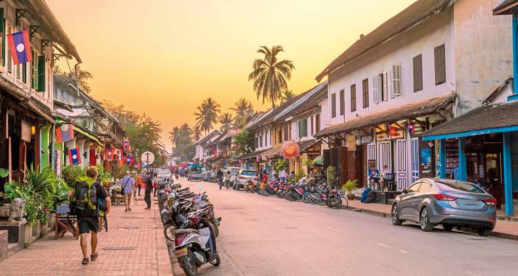 A bustling street with shops and motorbikes at sunset.