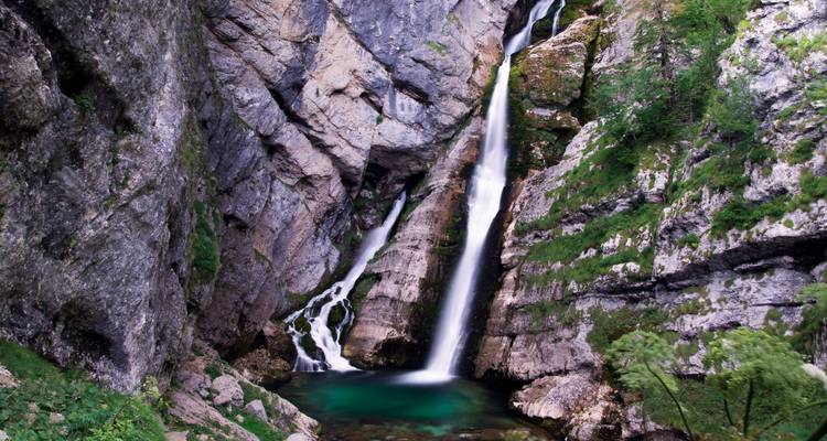 Une cascade gracieuse se jette dans un bassin turquoise entre des falaises rocheuses escarpées et mousseuses.