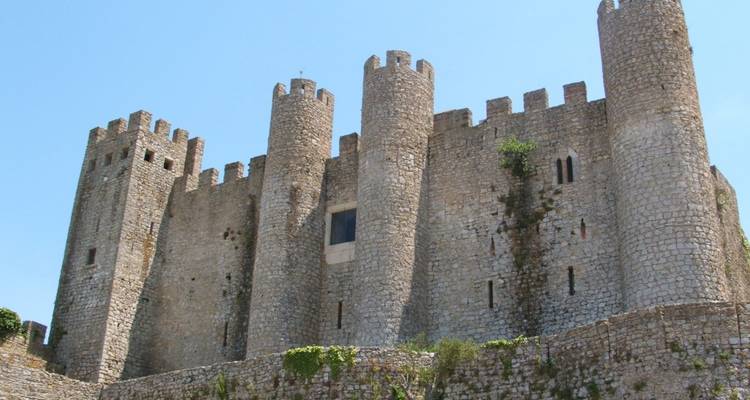 Stone battlements and turrets of Óbidos Castle rise against a clear sky.