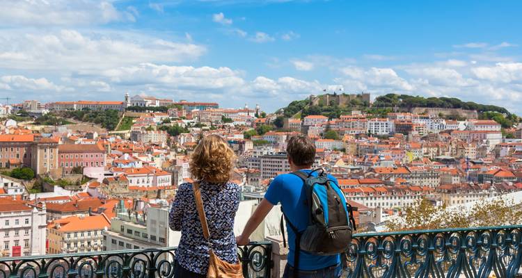 Couple gazes over Lisbon’s terracotta rooftops and São Jorge Castle from a wrought-iron viewpoint.