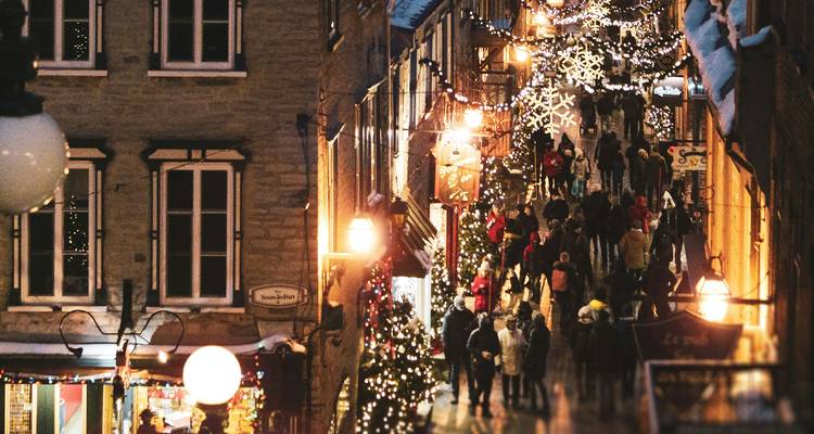 Rue charmante avec des décorations de Noël et des gens qui se promènent. Des lumières chaudes illuminent la scène.