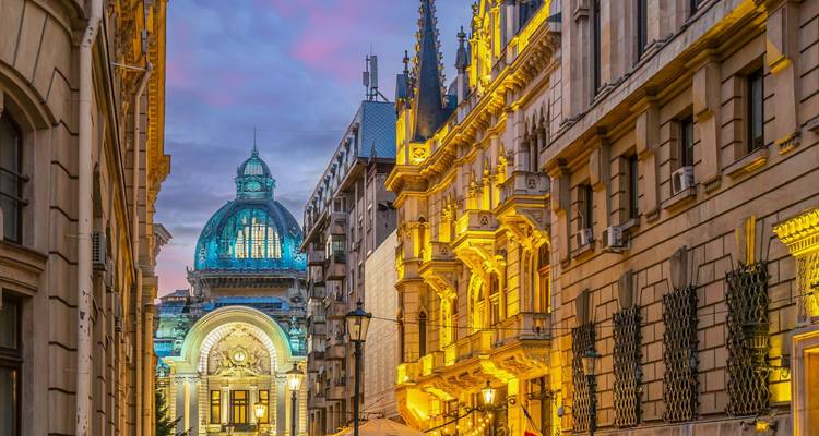 Escena nocturna de calle en Bucarest con la ornamentada cúpula del Palacio CEC iluminada contra un cielo pastel.