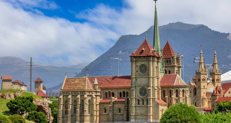 Complexe religieux avec cathédrale à flèche encadré par les montagnes.